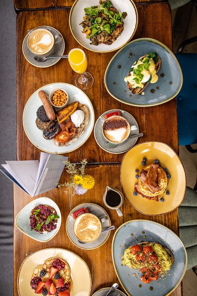 table full of plates of breakfast options and coffees